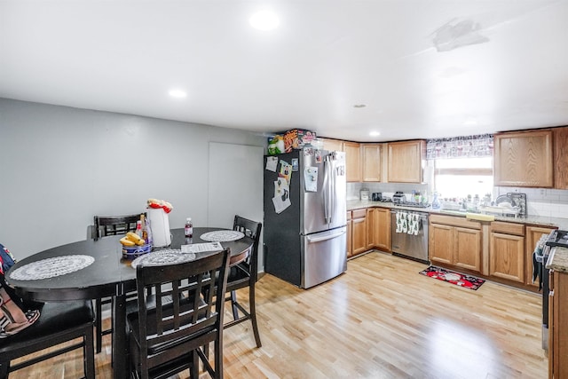 kitchen with tasteful backsplash, sink, appliances with stainless steel finishes, and light hardwood / wood-style flooring