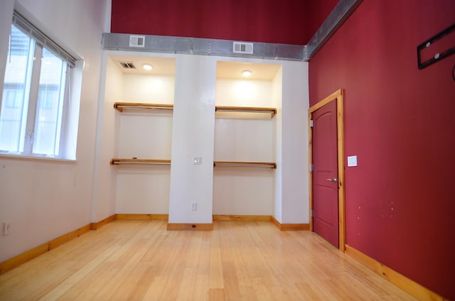 unfurnished bedroom featuring visible vents, multiple windows, two closets, and wood finished floors