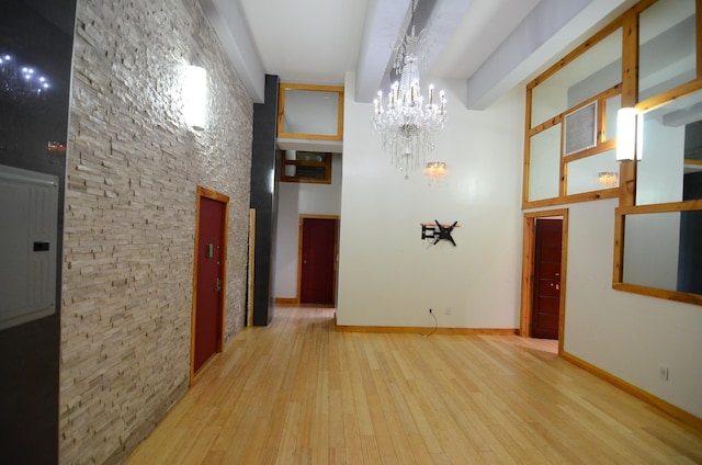 corridor featuring baseboards, a chandelier, hardwood / wood-style floors, beam ceiling, and a towering ceiling