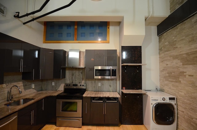 kitchen featuring backsplash, appliances with stainless steel finishes, washer / clothes dryer, wall chimney exhaust hood, and a sink