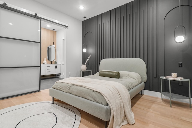 bedroom with light wood-type flooring, recessed lighting, and a barn door