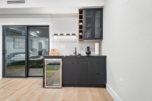 bar featuring baseboards, wine cooler, refrigerator, light wood-style floors, and a sink