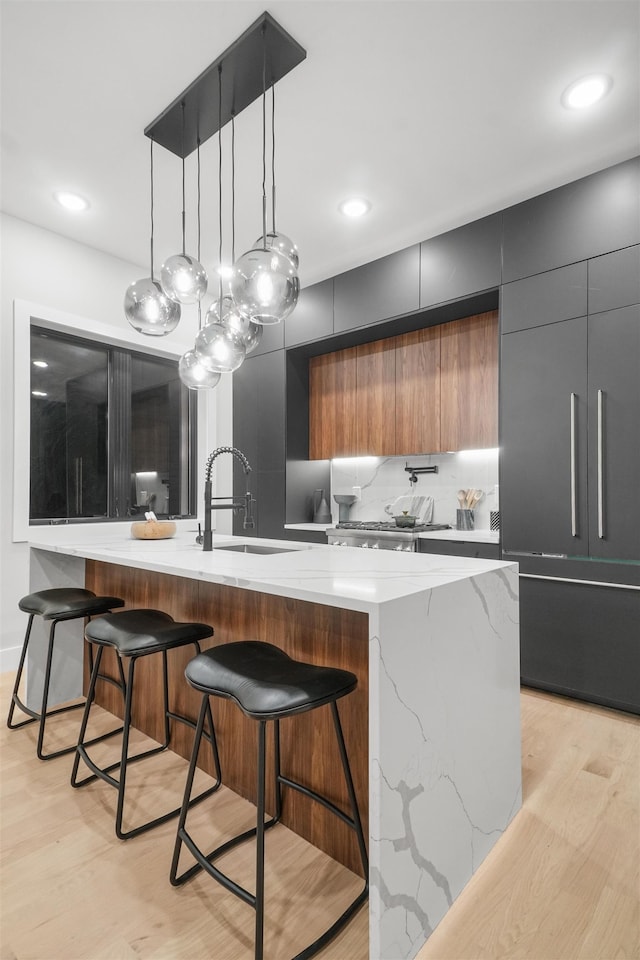 kitchen with hanging light fixtures, modern cabinets, a sink, and light wood-style flooring