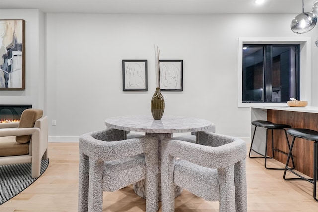 dining room with light wood-style floors, baseboards, and a glass covered fireplace