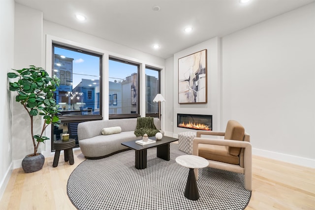 living area with baseboards, a glass covered fireplace, wood finished floors, and recessed lighting