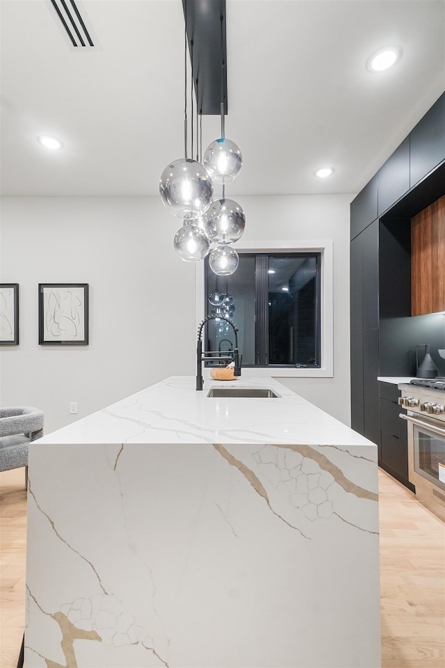 kitchen featuring high end stainless steel range oven, a sink, modern cabinets, dark cabinets, and light wood-type flooring