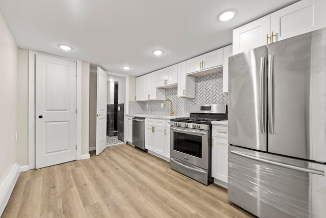 kitchen featuring light wood finished floors, backsplash, light countertops, stainless steel appliances, and white cabinetry