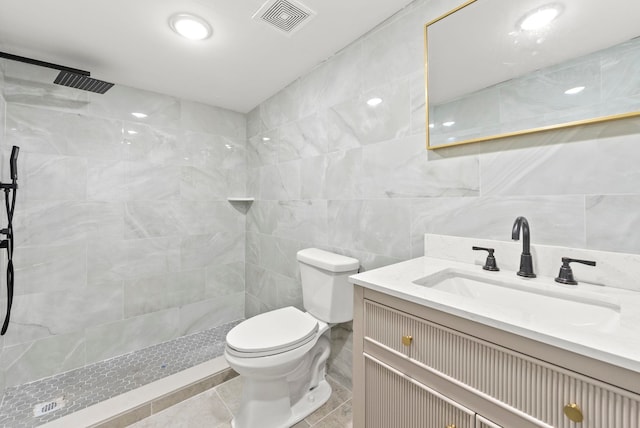 full bath featuring visible vents, toilet, vanity, tiled shower, and tile walls