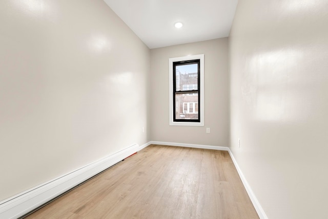 spare room with a baseboard heating unit, baseboards, and light wood finished floors