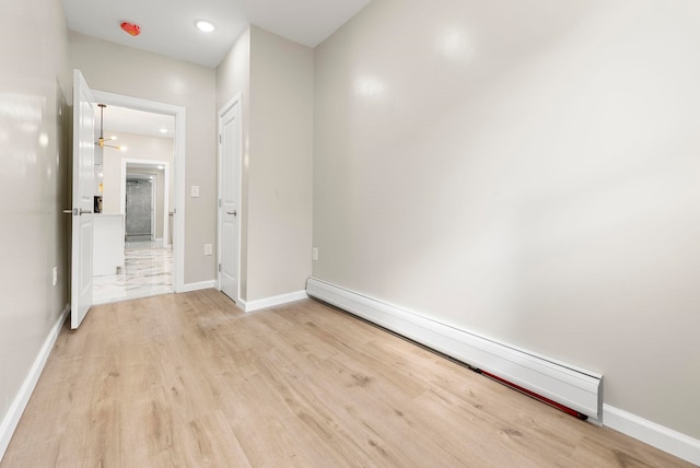 spare room with light wood finished floors, recessed lighting, a baseboard heating unit, and baseboards