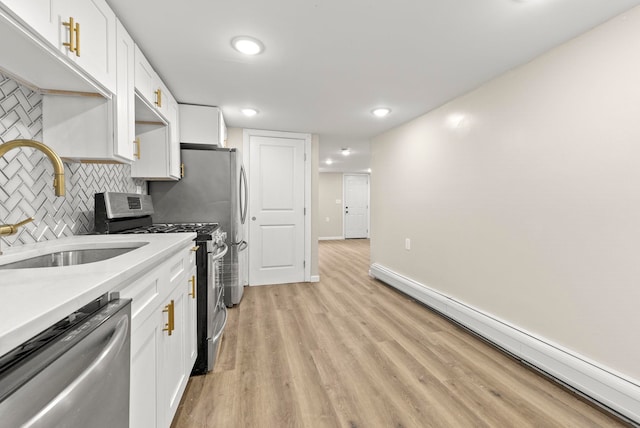 kitchen with a sink, stainless steel appliances, a baseboard heating unit, and white cabinets