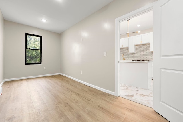 unfurnished room with recessed lighting, light wood-type flooring, baseboards, and a sink