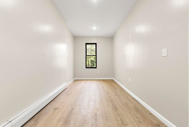 empty room featuring a baseboard heating unit, baseboards, and light wood finished floors