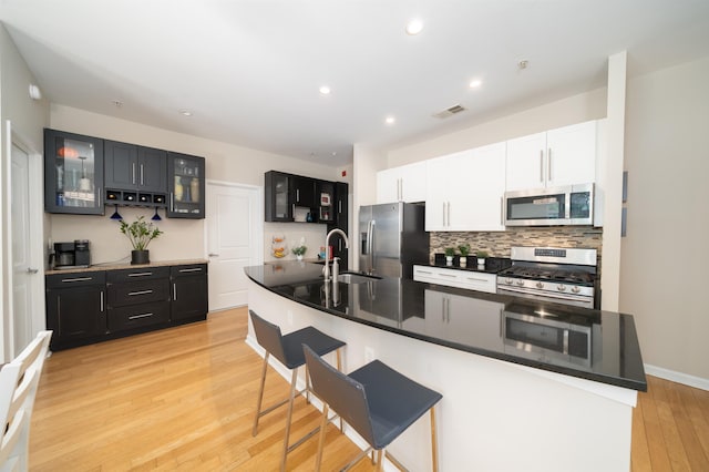 kitchen featuring stainless steel appliances, a sink, light wood-style flooring, backsplash, and a kitchen bar