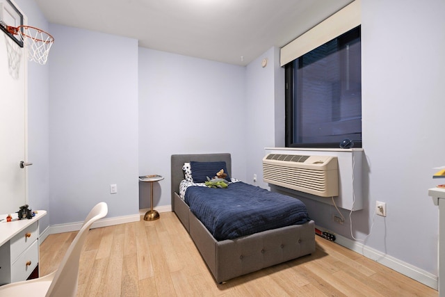 bedroom featuring light wood-type flooring, a wall mounted air conditioner, and baseboards