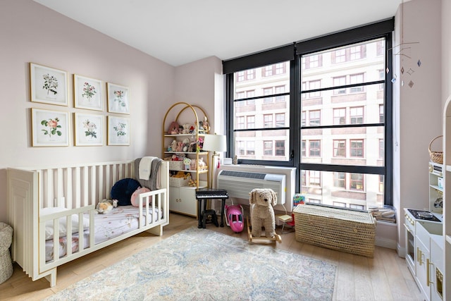 bedroom featuring a crib, a wall unit AC, wood finished floors, and floor to ceiling windows