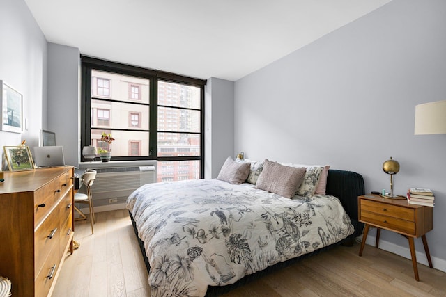 bedroom featuring light wood-style flooring, expansive windows, baseboards, and a wall mounted air conditioner