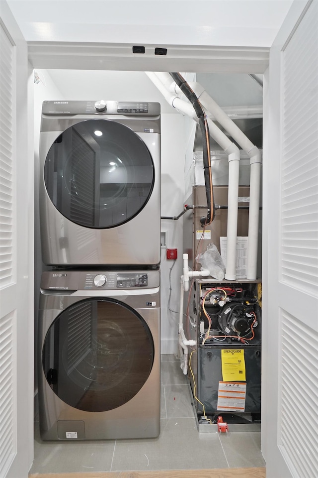 clothes washing area featuring stacked washer and clothes dryer, laundry area, and tile patterned flooring