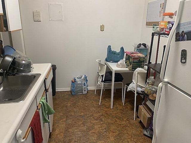 kitchen with freestanding refrigerator, baseboards, and a sink