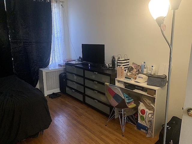 bedroom featuring multiple windows, wood finished floors, and radiator heating unit