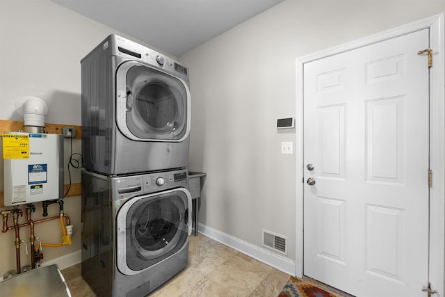 clothes washing area featuring stacked washer and dryer, water heater, laundry area, baseboards, and visible vents