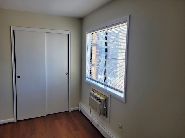 unfurnished bedroom with dark hardwood / wood-style floors, a baseboard radiator, a closet, and an AC wall unit