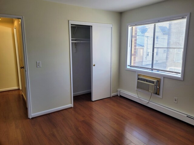 unfurnished bedroom with a baseboard radiator, a closet, an AC wall unit, and dark hardwood / wood-style flooring