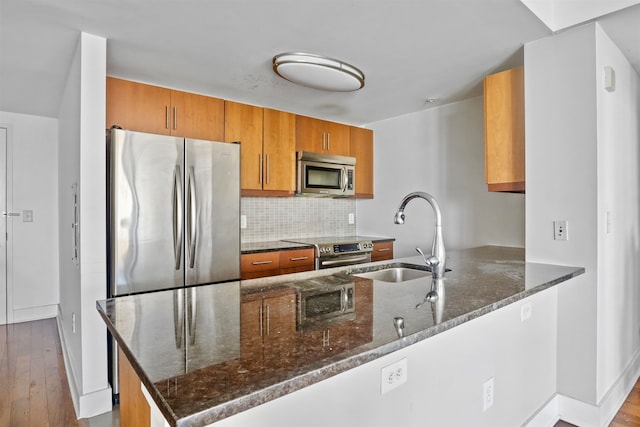 kitchen featuring stainless steel appliances, kitchen peninsula, sink, light wood-type flooring, and dark stone countertops