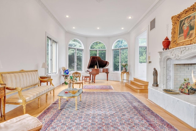 living area with ornamental molding, light wood-type flooring, and a high end fireplace