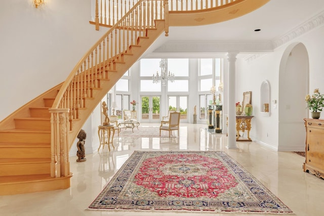 entrance foyer with an inviting chandelier, french doors, ornate columns, and a towering ceiling