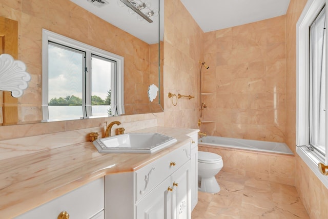 full bathroom with toilet, tiled shower / bath combo, vanity, and tile walls