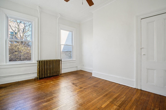 unfurnished room featuring hardwood / wood-style flooring, a ceiling fan, baseboards, ornamental molding, and radiator heating unit