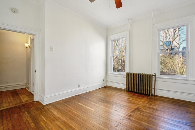 empty room with radiator, a healthy amount of sunlight, wood-type flooring, and baseboards