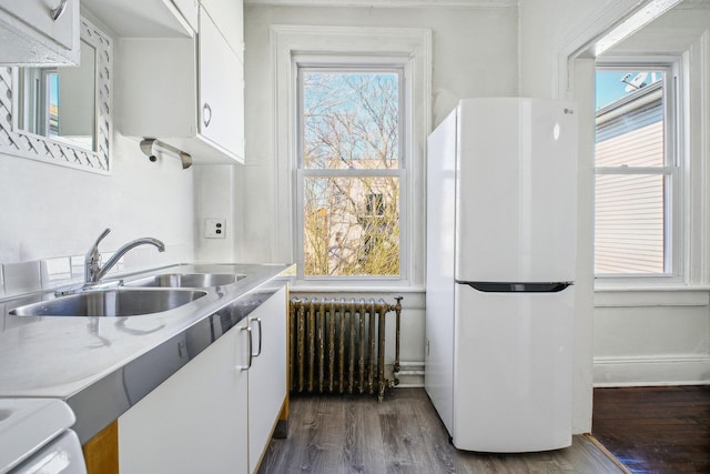 kitchen featuring white cabinets, radiator, freestanding refrigerator, light countertops, and a sink