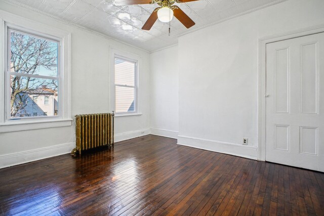 spare room featuring baseboards, a ceiling fan, radiator, hardwood / wood-style flooring, and an ornate ceiling