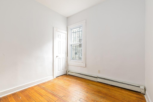 empty room with a baseboard heating unit, light wood-type flooring, and baseboards