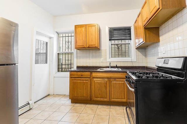 kitchen with brown cabinets, dark countertops, a sink, appliances with stainless steel finishes, and baseboard heating
