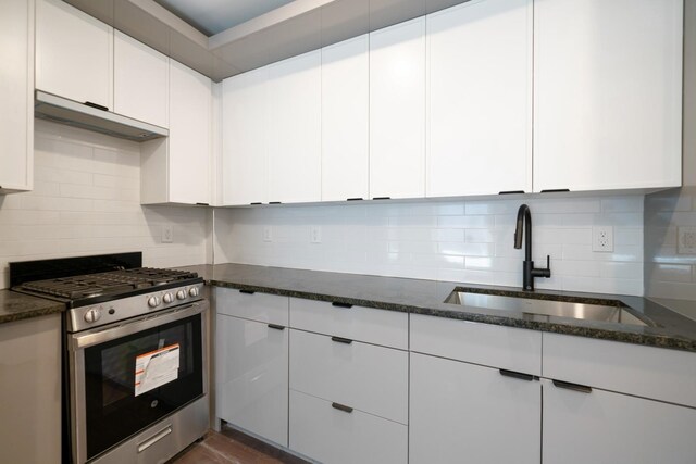 kitchen featuring decorative backsplash, sink, stainless steel gas stove, white cabinetry, and dark stone countertops