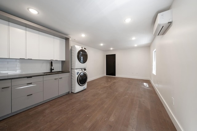 laundry area with dark hardwood / wood-style flooring, stacked washing maching and dryer, a wall unit AC, and sink