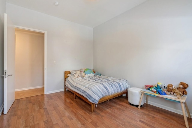 bedroom with light wood-type flooring, baseboards, and lofted ceiling