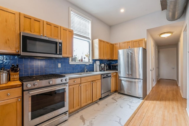 kitchen featuring a sink, marble finish floor, light countertops, appliances with stainless steel finishes, and decorative backsplash