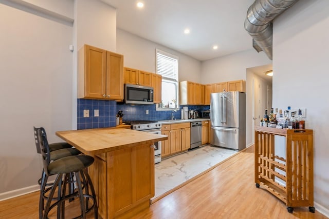 kitchen featuring premium appliances, butcher block countertops, a breakfast bar, baseboards, and decorative backsplash