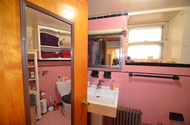 bathroom with toilet, radiator heating unit, a sink, and tile walls