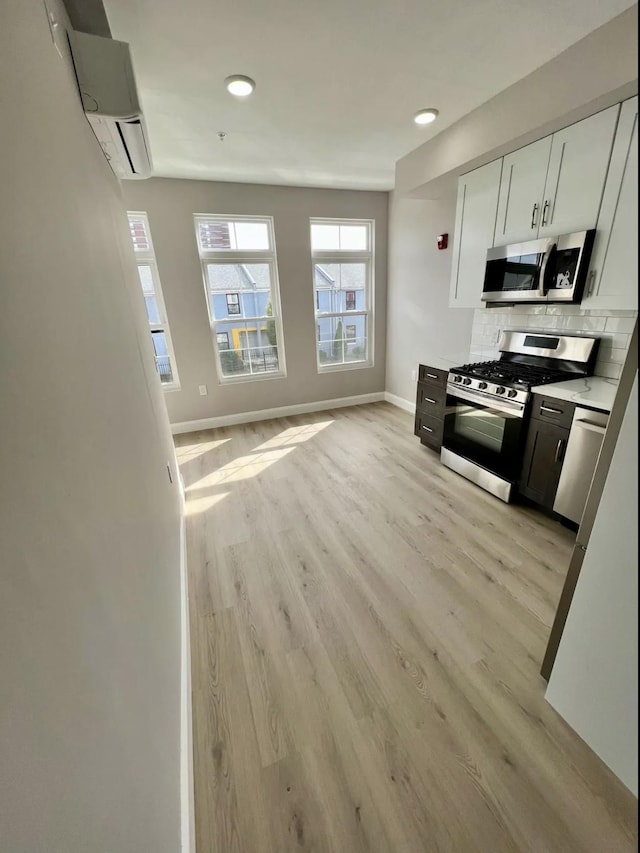 kitchen featuring white cabinetry, backsplash, stainless steel appliances, light hardwood / wood-style floors, and an AC wall unit