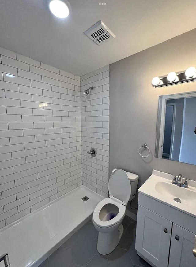 bathroom with tile patterned flooring, vanity, tiled shower, and toilet