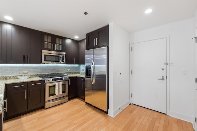 kitchen with stainless steel appliances, backsplash, light stone counters, and light wood finished floors