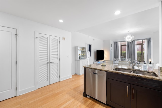 kitchen with dishwasher, a sink, light wood-style floors, and light stone counters