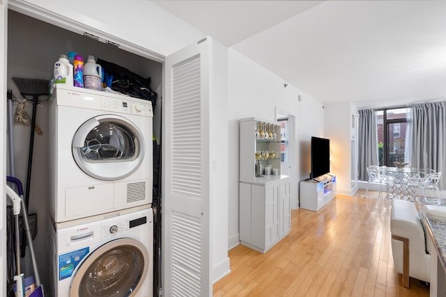 clothes washing area with baseboards, light wood-type flooring, stacked washer / drying machine, and laundry area