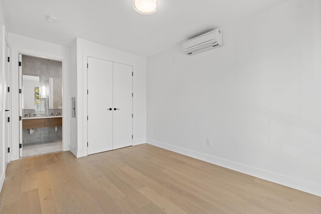 unfurnished bedroom with light wood-type flooring, a closet, ensuite bath, and a wall mounted AC