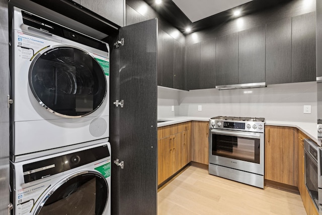 kitchen with high end stainless steel range, stacked washing maching and dryer, extractor fan, and light wood-type flooring